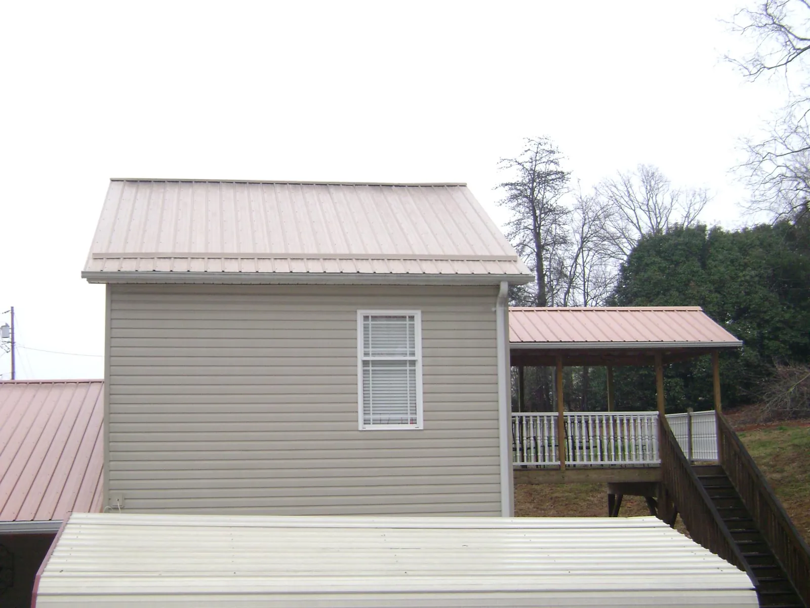 Tan metal roofs on a two story addition and attached porch, from a Roof Replacement job in Warren